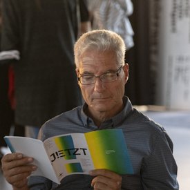 Ein männlich gelesener Gast blättert im Programmheft des Festival JETZT!