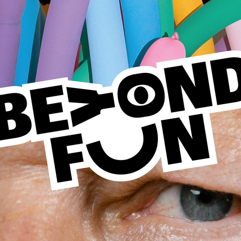 Nahaufnahme eines Gesichts mit blauen Augen und bunten Luftballons im Hintergrund sowie dem Schriftzug 'BEYOND FUN' in Schwarz-Weiß über den Augen