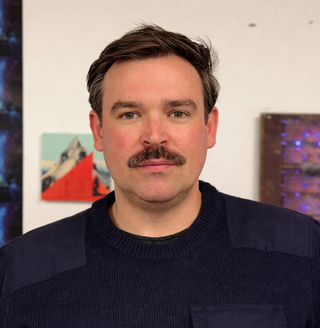 Clair Bötschi: Mann mit dunklem Pullover vor einer Wand mit mehreren bunten Bildern