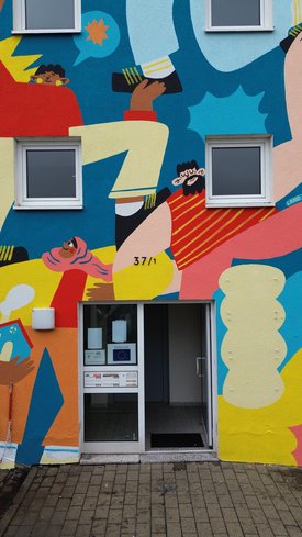 Das Foto zeigt einen Hauseingang. Die Fassade des Hauses ist bunt bemalt.