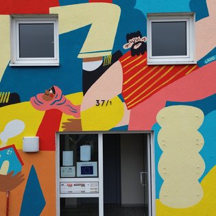 Das Foto zeigt einen Hauseingang. Die Fassade des Hauses ist bunt bemalt.