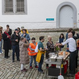 Vor dem Stand der Food Performance von Marcus Bergmann hat sich eine lange Menschenschlange gebildet. Marcus Bergmann steht an einem Tisch mit Küchenutensilien und verteilt Pizza.