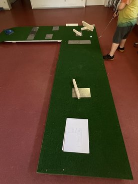 Minigolfbahn mit grünem Teppich, Holzhindernissen und einer Person, die einen Schläger hält