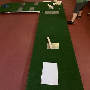 Minigolfbahn mit grünem Teppich, Holzhindernissen und einer Person, die einen Schläger hält