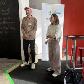 Melanie Müller und Markus Niessner von niessnerdesign stehen nebeneinander und sprechen zur Teilnehmergruppe, die aber nicht auf dem Bild zu sehen ist.