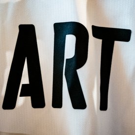 Große schwarze Buchstaben 'ART' auf weißem Stoff, leicht zerknittert. Ausschnitt aus einem Trikot des VfB Stuttgart.