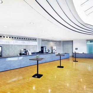 Innenansicht auf das Foyer. Die Wände sind in hellen Tönen gehalten, der Bereich verfügt über einen Parkettboden. 