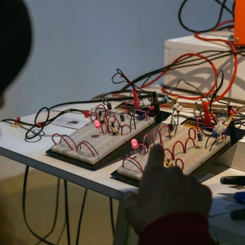 Person vor zwei Steckbrettern mit elektronischen Bauteilen und leuchtenden LEDs auf einem Tisch