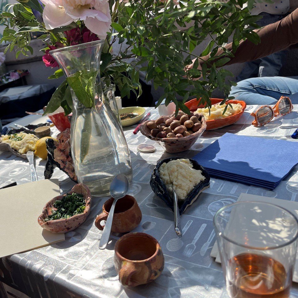Tisch mit verschiedenen Schalen und Tellern mit Lebensmitteln, einer Glasvase mit Blumen und mehreren Personen im Hintergrund