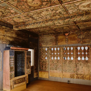 Prunkvoll bemalter Synagogeninnenraum mit farbenfrohen floralen Decken- und Wandmalereien, hebräischen Inschriften und einer geöffneten Toranische. Der Raum zeigt die kunstvolle Gestaltung jüdischer Sakralarchitektur aus vergangenen Jahrhunderten.