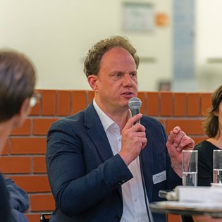 Dr. Matthias Knecht spricht auf dem Podium ins Mikrofon und gestikuliert mit der Hand