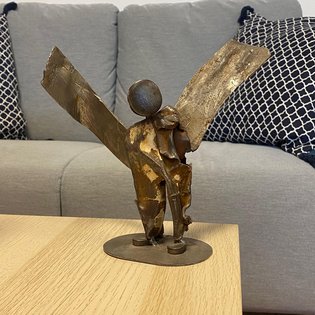 Foto der Plastik »Engel« von Susanne Von Rosen. Der Engel steht auf einem Holztisch. Im Hintergrund ist ein Sofa zu sehen.