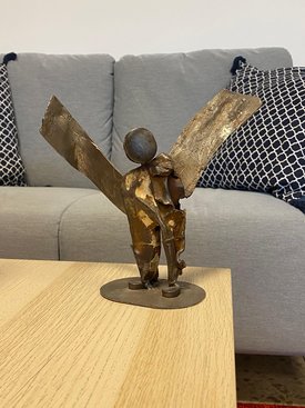 Foto der Plastik »Engel« von Susanne Von Rosen. Der Engel steht auf einem Holztisch. Im Hintergrund ist ein Sofa zu sehen.