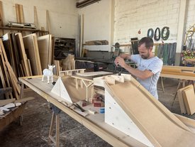 Mann baut in Werkstatt eine Minigolfbahn aus Holz mit Rampe und Ziegenfigur