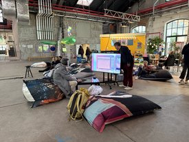 Teilnehmer entspannen auf Sitzsäcken und betrachten digitale Kunst auf einem Bildschirm beim Kunst-im-Game-Symposium.
