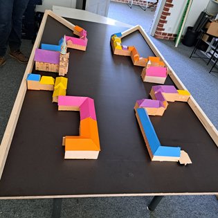 Modell einer Minigolfbahn mit bunten, kleinen Gebäuden auf schwarzer Spielfläche in einem Raum mit Teppichboden