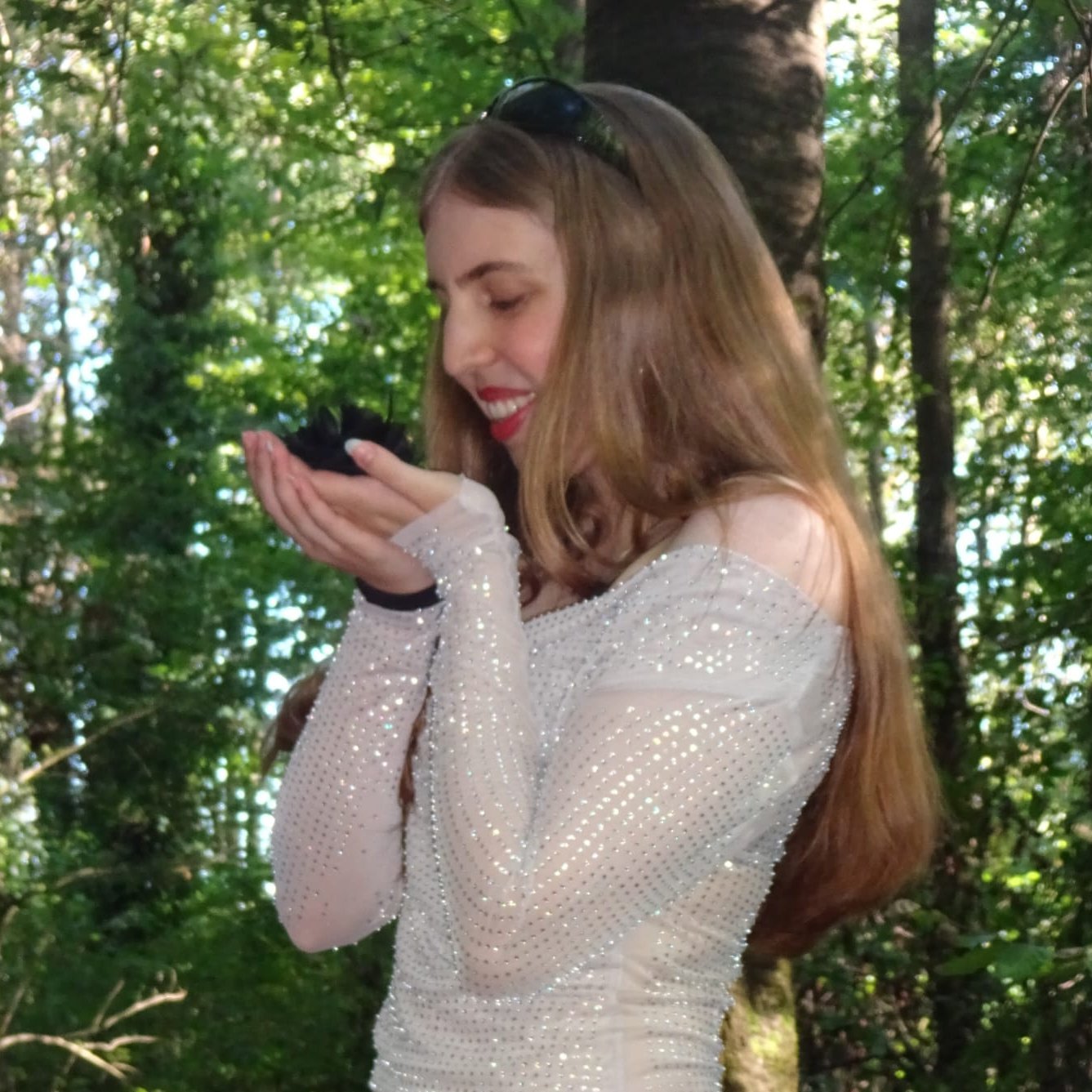 Junge Frau mit langem Haar, weißem, schulterfreiem Oberteil und Jeans steht im Wald und hält die Hände vor dem Gesicht