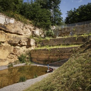 Ein kleines Kind schaut auf einen kleinen See im Travertinpark. Der See ist von Gesteinskanten des Steinbruchs umgeben.