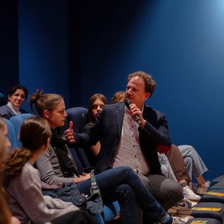 Dr. Matthias Knecht sitzt in der ersten Reihe und hat sich mit einem Mikrofon in der Hand dem restlichen Publikum zugewandt.