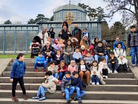Gruppenbild von mehreren Personen, die auf einer Treppe stehen oder sitzen - hauptsächlich Kinder. Im Hintergrund ist ein Gebäude zu sheen, bei dem es sich um ein Gewächshaus handeln könnte.