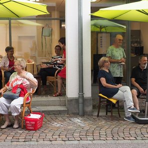 Menschen sitzen unter Sonnenschirmen vor den Café SprechZimmer