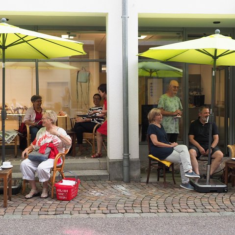 Menschen sitzen unter Sonnenschirmen vor den Café SprechZimmer