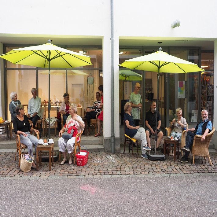 Menschen sitzen unter Sonnenschirmen vor den Café SprechZimmer