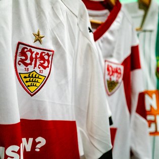 Weiße Trikots mit rotem Querstreifen und dem Vereinswappen von VfB Stuttgart, das eine goldene Sternapplikation trägt.