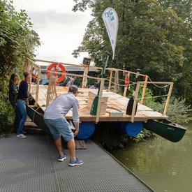 Mehrere Personen lassen das Festival-Floß zu Wasser.