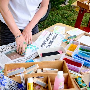 auf einem bunten Basteltisch sind verschiedene Stempel mit Wörtern aus verschiedenen Sprachen zu sehen: FReiheit, Utopie, Gemeinschaft
