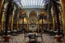 Innenraum der Maurischen Halle im Palais Thermal Bad Wildbad mit Säulen, Palmen in Töpfen und Tischen mit Stühlen auf einem gemusterten Boden unter einem Glasdach