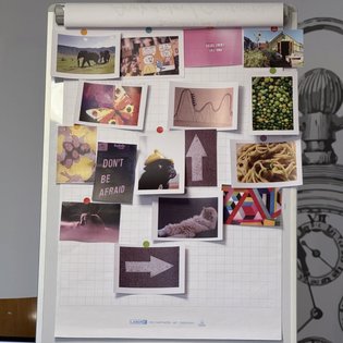 Bild eines Flipcharts, auf das mehrere kleinere Fotos geklebt sind. Es sind Fotos von Elefanten, Früchten, einem Schmetterling, einem Pfeil, einer Katze bei der Fellpflege und weiteren Motiven.