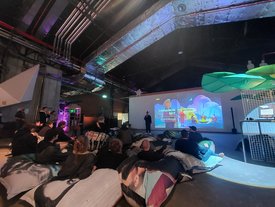 Teilnehmer des Symposiums in Stuttgart betrachten eine bunte Leinwandpräsentation zu Kunst im Gaming-Kontext.