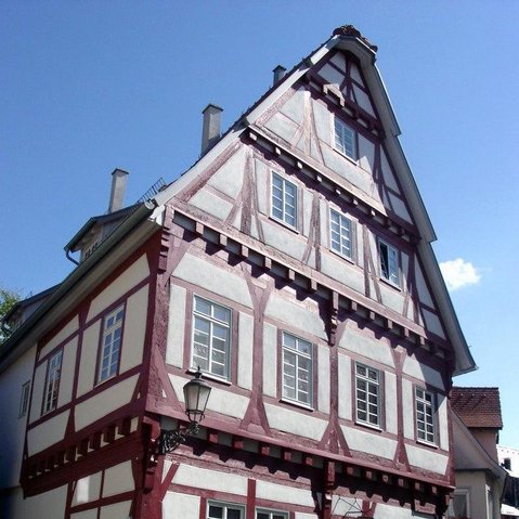 Ansicht eines Fachwerkhauses von außen. Das Gebälk ist in einem roten Ton gehalten. Der Hiimmel über dem Gebäude ist strahlend blau.