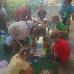 Kinder spielen im Freien an einem selbstgebauten Minigolf-Parcours aus bemalten Kartons und Holzklötzen