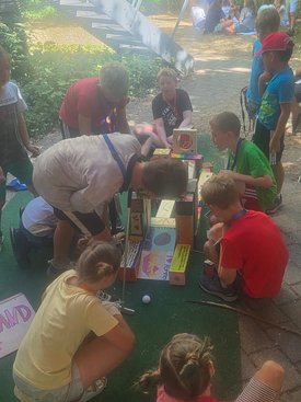 Kinder spielen im Freien an einem selbstgebauten Minigolf-Parcours aus bemalten Kartons und Holzklötzen