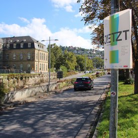 Ein Plakat von JETZT! hängt an einem Laternenmast an einer Straße vor dem neuen Schloss in Stuttgart.