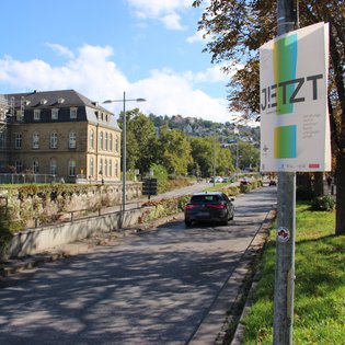 Ein Plakat von JETZT! hängt an einem Laternenmast an einer Straße vor dem neuen Schloss in Stuttgart.