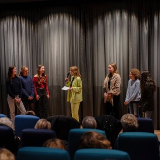 Moderatorin Viktoria Merkulova im Gespräch mit fünf Schüler*innen auf der Bühne vor der Kinoleinwand.