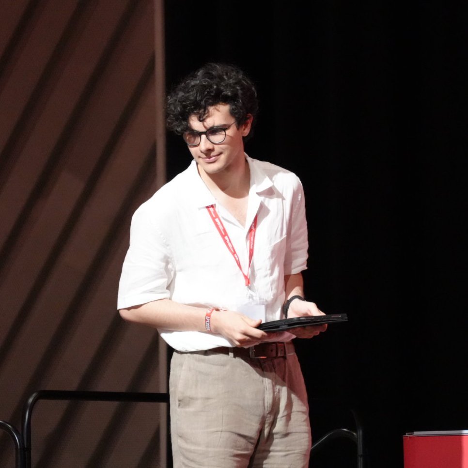 Junger Mann mit Brille und weißem Hemd steht mit Tablet in der Hand vor einem Podium auf einer Bühne