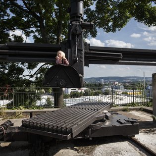 Ein kleines Kind klettert auf einer stillgelegten Bergbauanlage. Im Hintergrund ist vermutlich Bad Cannstatt zu sehen.