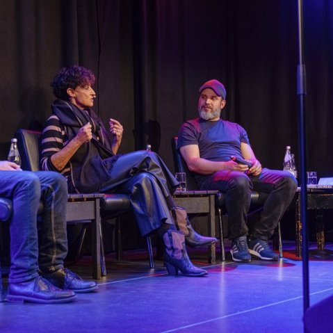 Blick auf die Bühne mit den Podcast-Gästen und -Moderator