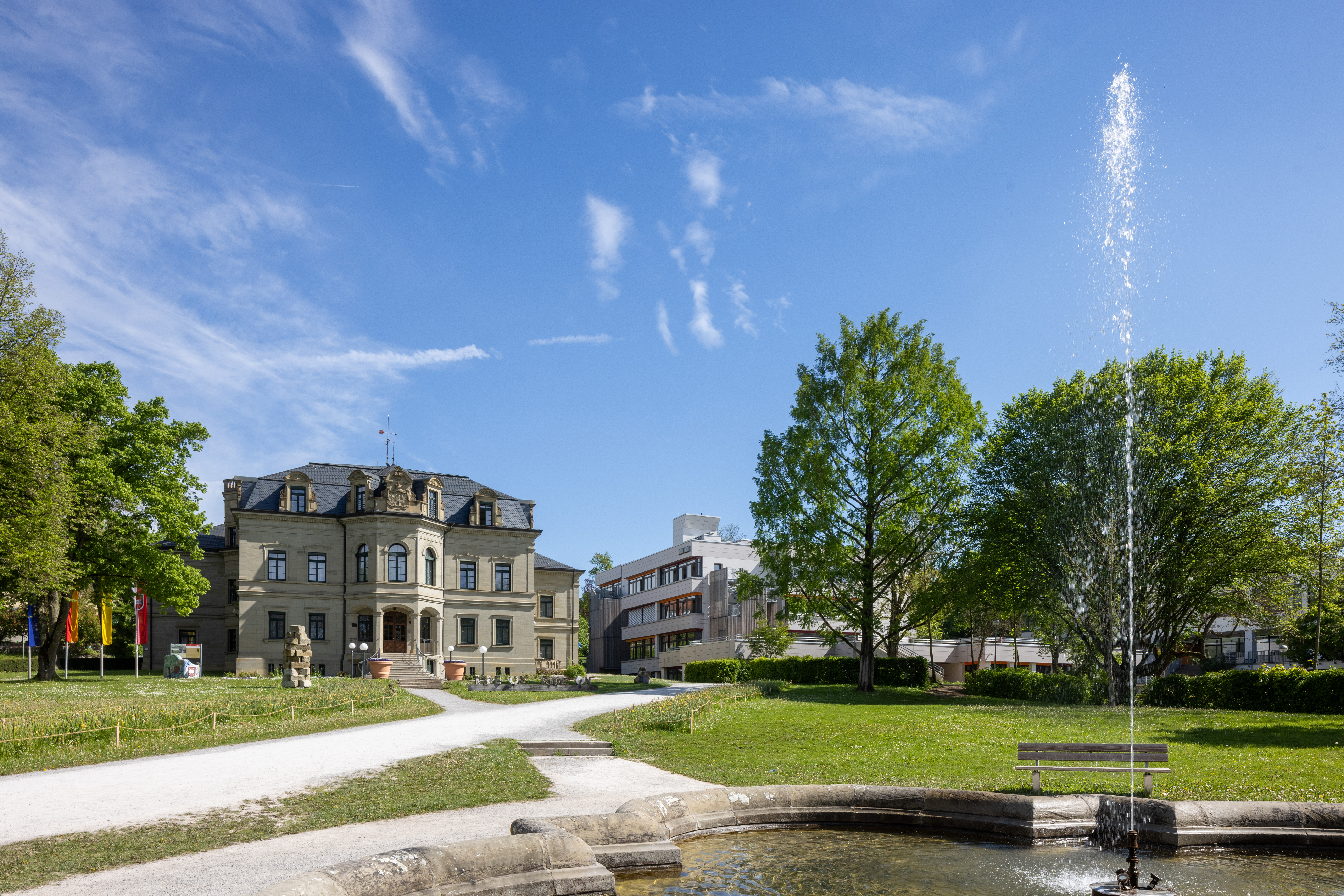Historisches Rathausgebäude mit Park, Springbrunnen und Bänken bei klarem Himmel
