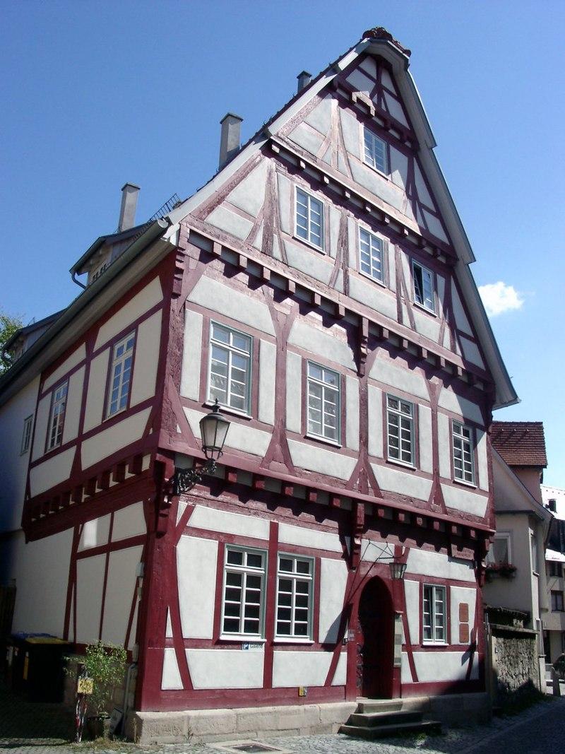 Ansicht eines Fachwerkhauses von außen. Das Gebälk ist in einem roten Ton gehalten. Der Hiimmel über dem Gebäude ist strahlend blau.