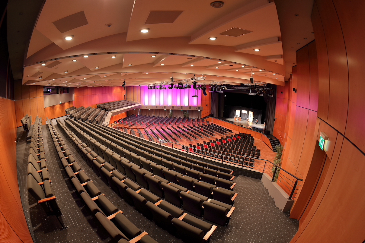 Innenansicht der Kongresshalle: über Stuhlreihen hinweg wird auf eine Bühne geblickt.