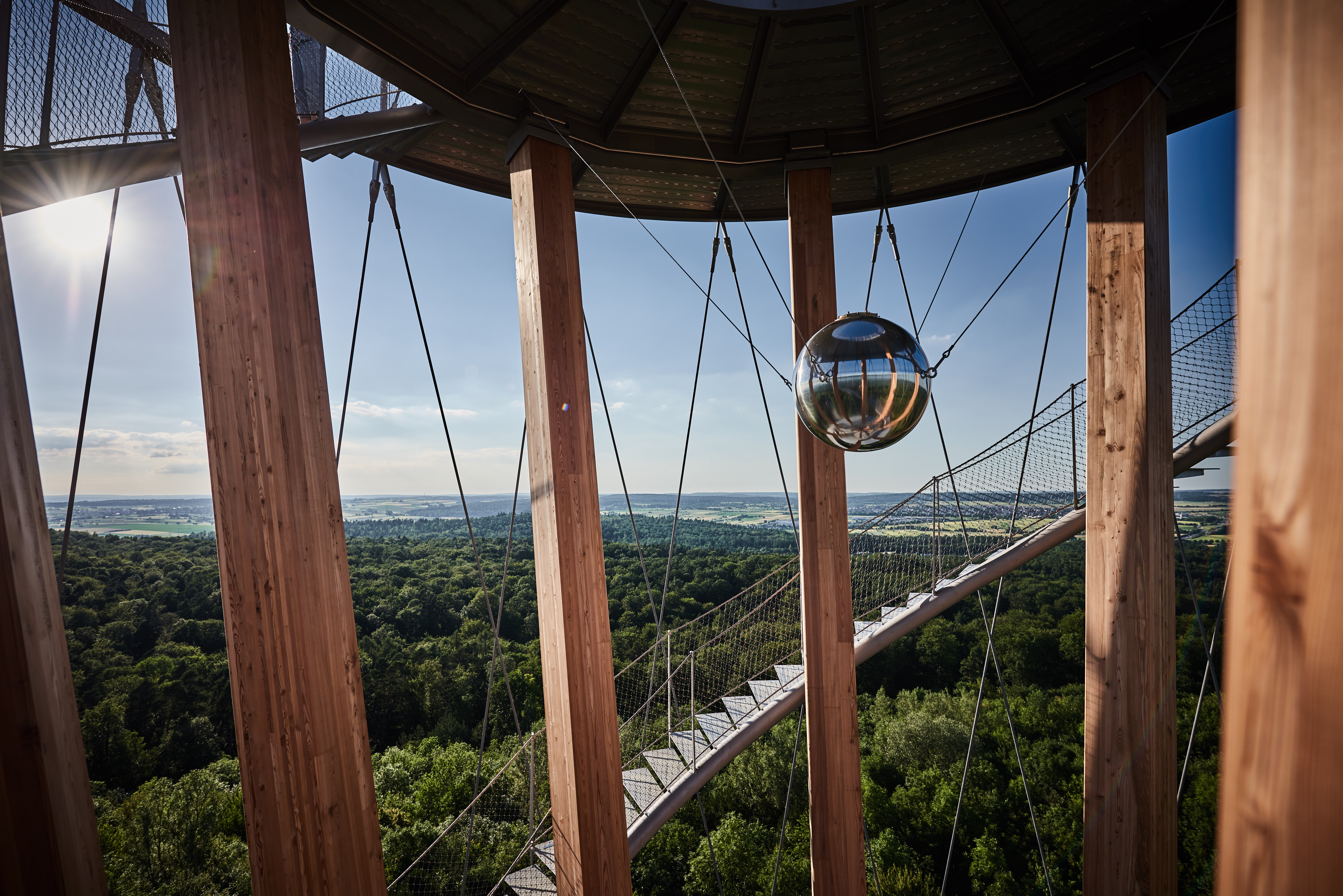 Foto: Blick durch die Säulen des Turmes hindurch in die weite Landschaft. Im vordergrund ist Wald zu sehen. Weiter hinten weitere Wälder, Felder und Ortschaften.