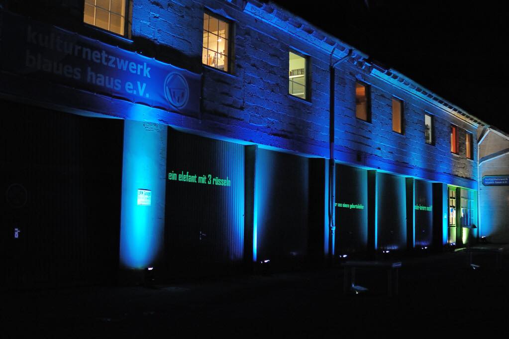 Aussenansicht blaues Haus. Die Fassade ist mit blauem Licht beleuchtet.